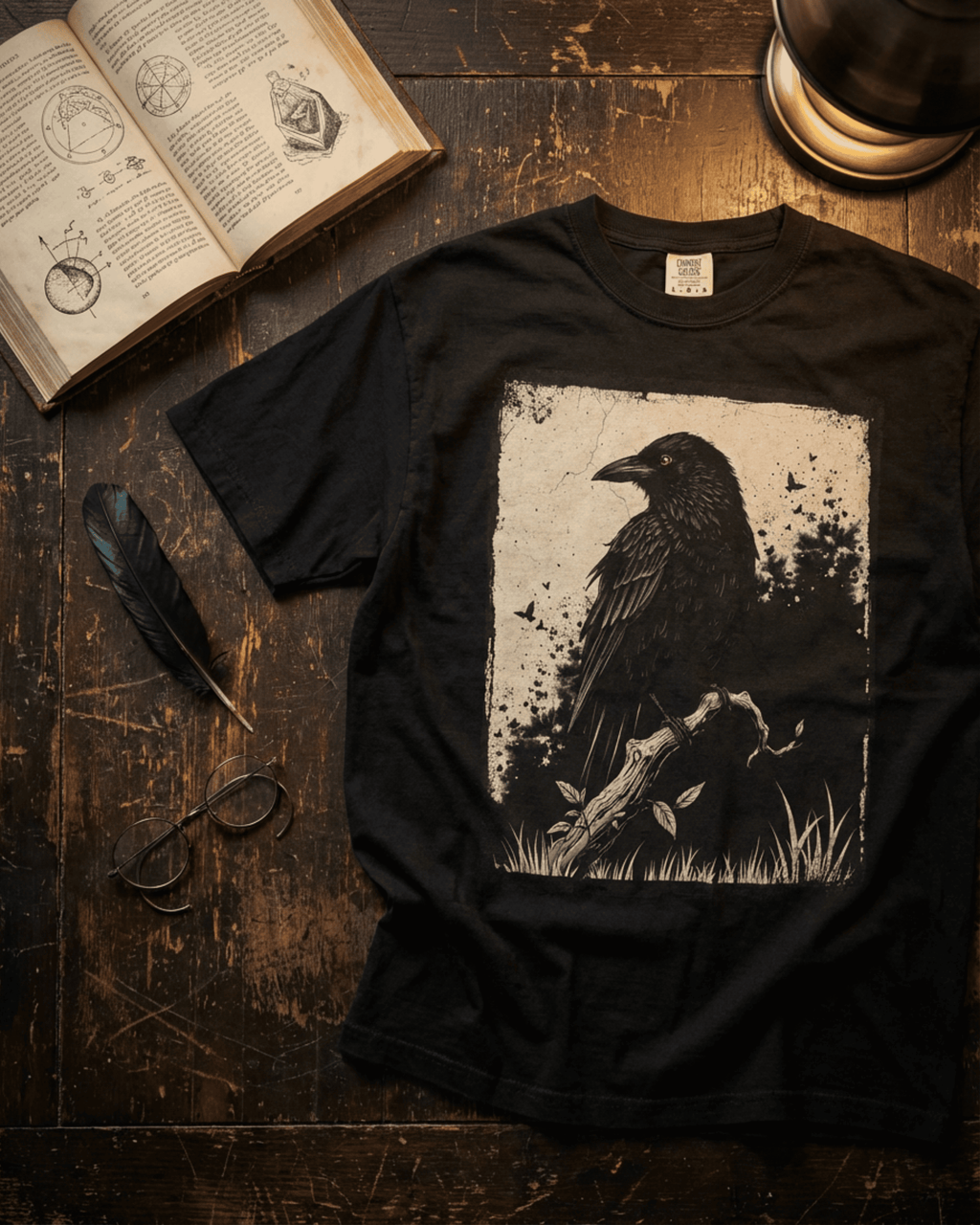  A flat lay of the Comfort Colors Black Raven Tshirt on a rustic wooden desk. This Dark Academia aesthetic tee is styled in a scholarly setting with an open vintage book, a black feather quill, and wire-rimmed glasses, creating a moody and intellectual vibe.