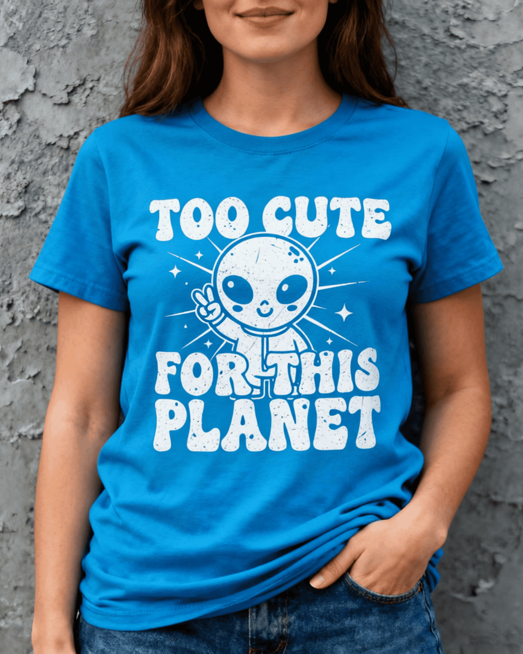 A woman models a vibrant blue Cute Alien Peace Sign T-Shirt. The funny graphic tee features a friendly alien with the retro text 'Too Cute For This Planet,' making it a perfect Outer Space Lover TShirt for women.