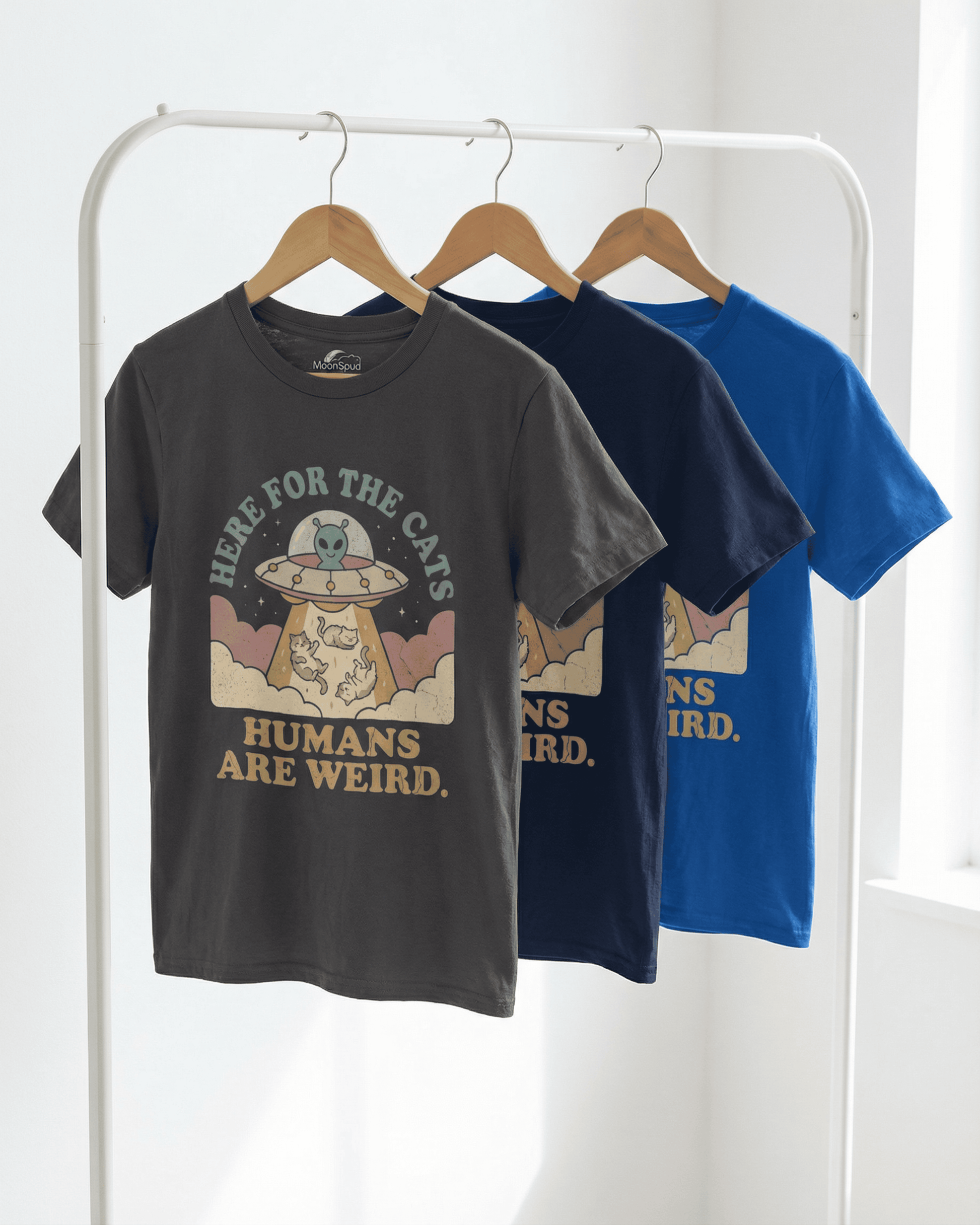 Front view of the 'Here for the Cats' cute kids alien cat t-shirt in a charcoal grey color, hanging on a rack. The retro 'Humans Are Weird' graphic tee design features a UFO with an alien beaming up happy cats.