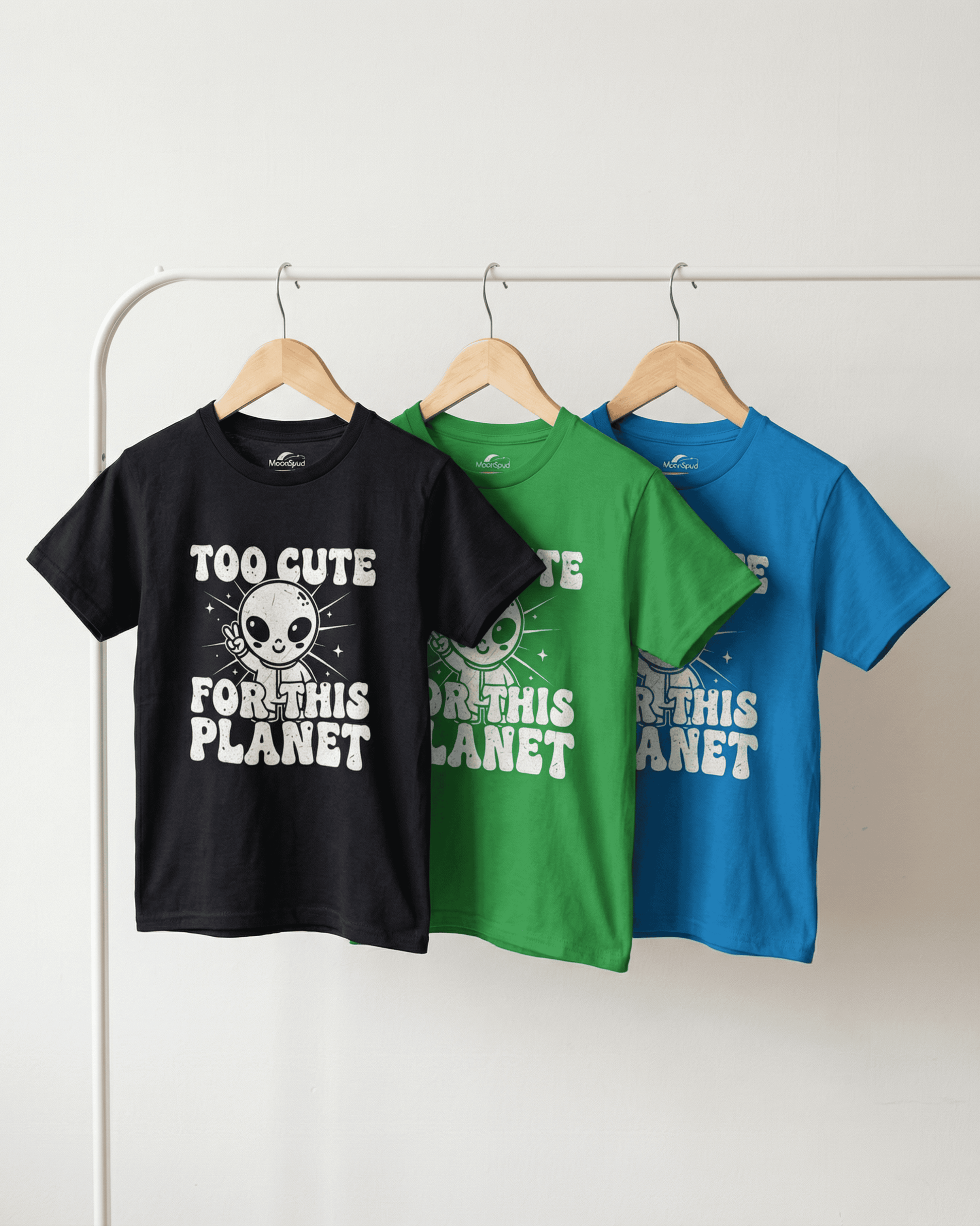 A side view of the black, green, and blue cute kids alien tshirt options hanging on a white clothing rack. This clean product shot shows the quality and fit of the funny youth apparel, perfect for any space-loving child.