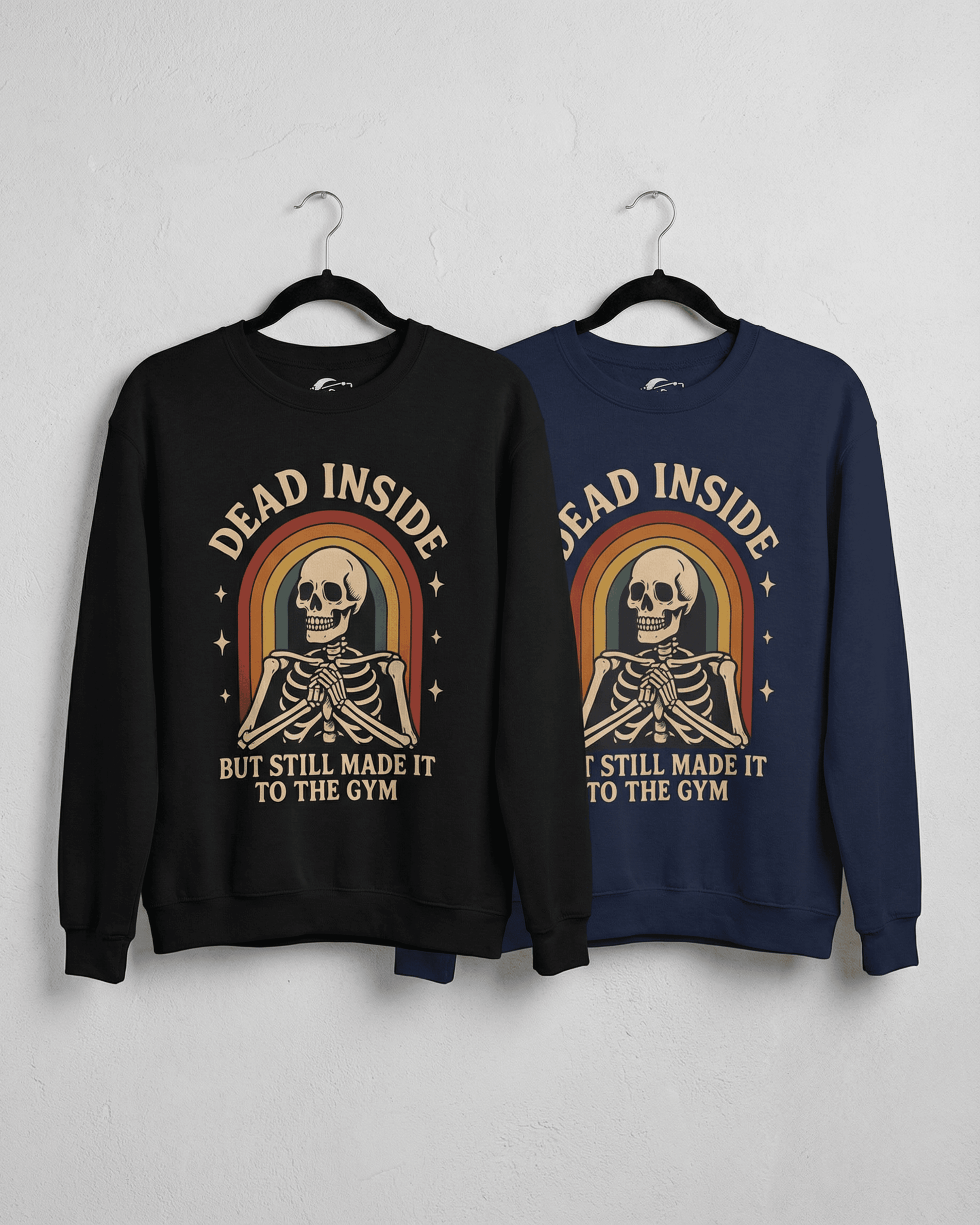 A black and a navy blue Funny Retro Gym Sweatshirt hanging side-by-side to show color options. Both Rainbow Skeleton Dead Inside Pullovers feature the same humorous 'Dead Inside But Still Made It To The Gym' design.