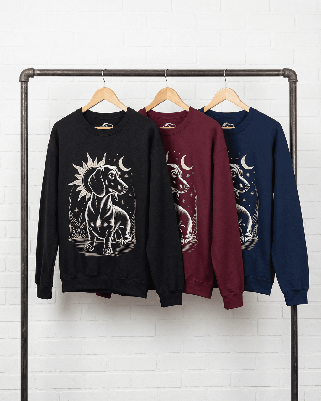 A Doxie lover crewneck top shown in three colors (black, maroon, and navy) hanging on a clothing rack. This sweatshirt is a perfect gift for a dog mom and features a stylish 'long dog' aesthetic with a celestial dachshund design.