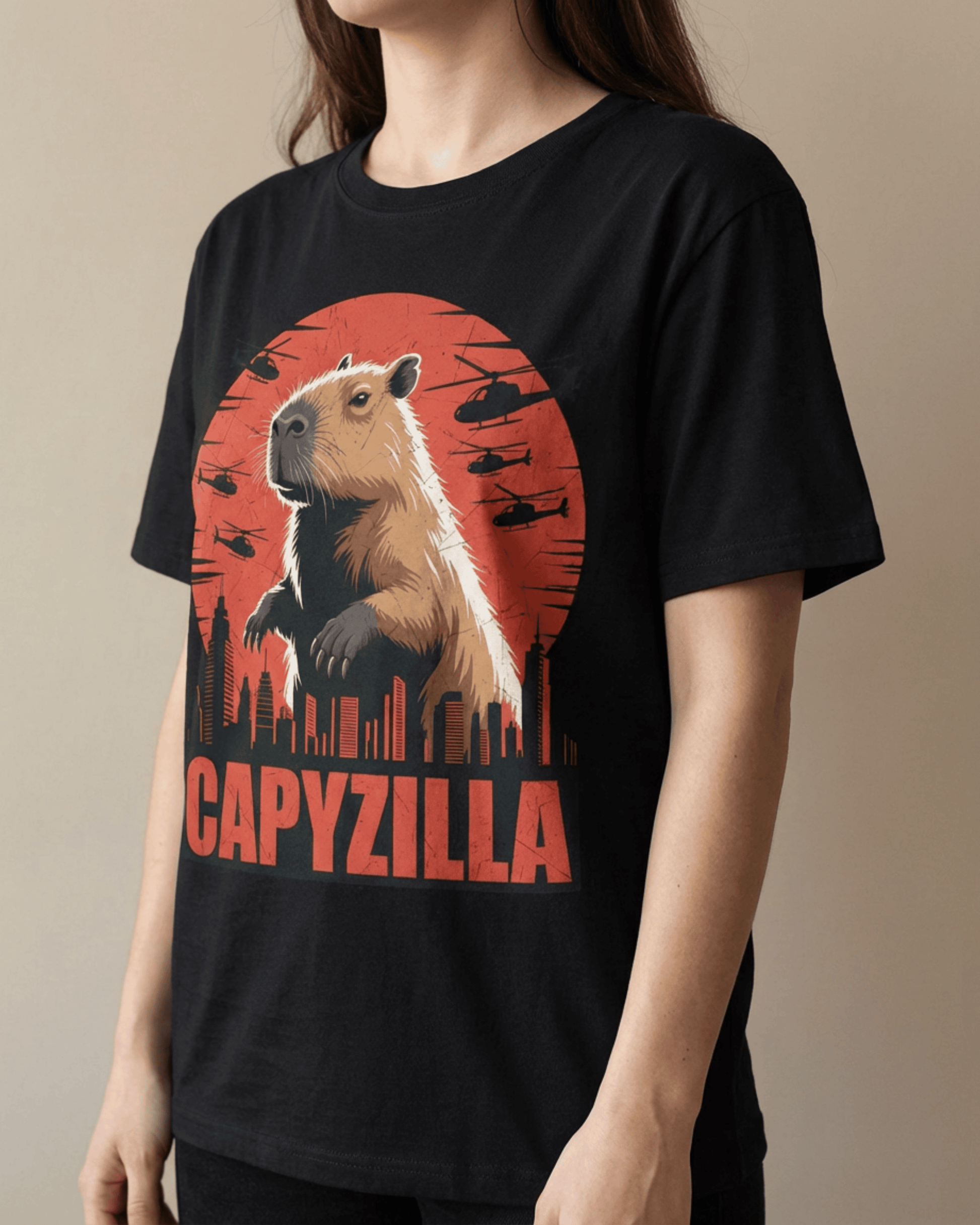 A female model wearing a comfortable black Funny Capybara Monster T-Shirt. The striking 'CAPYZILLA' Godzilla Parody graphic prominently features a massive capybara standing amidst a city skyline, silhouetted by a vivid red sunset and surrounded by flying helicopters. This shot emphasizes the flattering fit and eye-catching design of the graphic tee, perfect for a casual look.