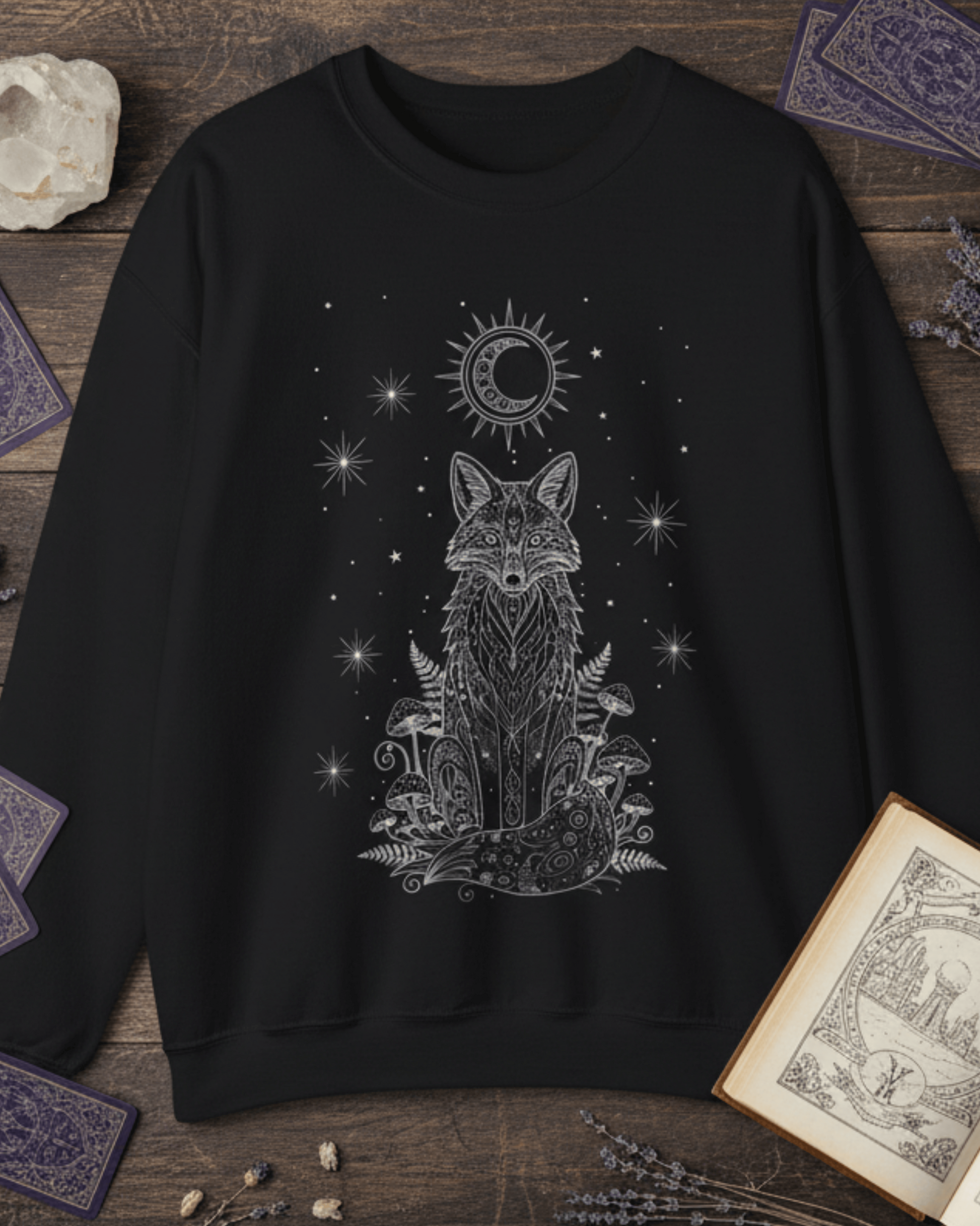 Flat lay of the black Fox Celestial Moon Sweatshirt, styled to showcase its witchy aesthetic with tarot cards, a crystal, and dried lavender on a dark wood surface.