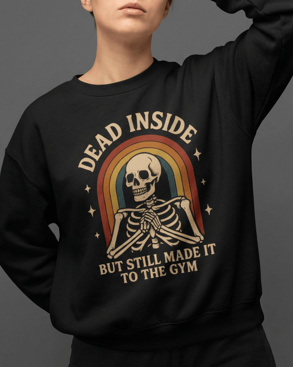 A woman models a black Funny Retro Gym Sweatshirt with a vintage-inspired design. The graphic features a cheerful skeleton in front of a 70s-style rainbow, making it a perfect Rainbow Skeleton Dead Inside Pullover for a humorous workout.