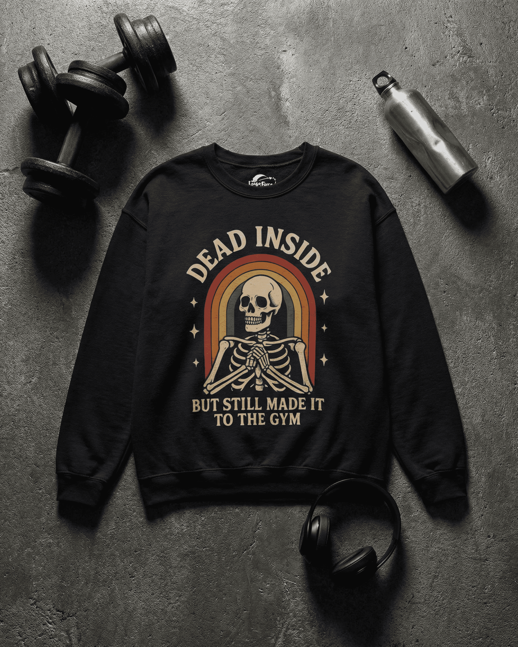 A flat lay of a black Funny Retro Gym Sweatshirt on a dark concrete floor, surrounded by workout gear including dumbbells and a water bottle. The Rainbow Skeleton Dead Inside Pullover graphic is centered, highlighting its fitness-related humor.