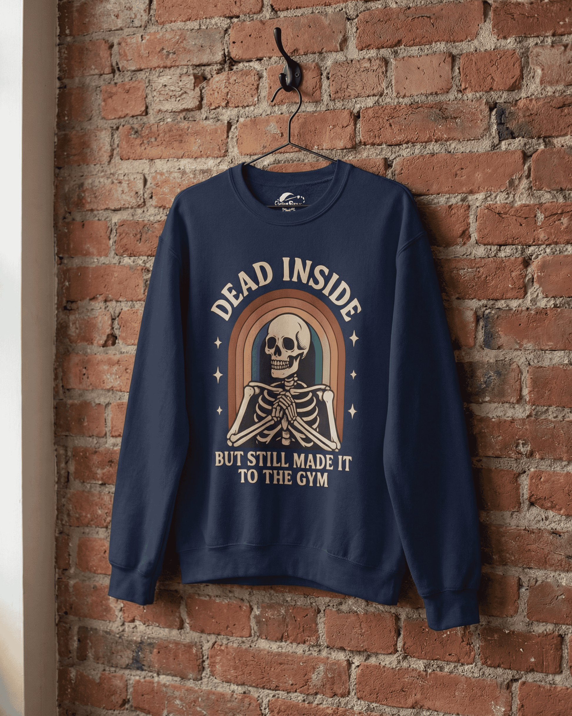 The navy Funny Retro Gym Sweatshirt hanging from a hook on a rustic red brick wall. This product shot showcases the high-quality print of the Rainbow Skeleton Dead Inside Pullover graphic.