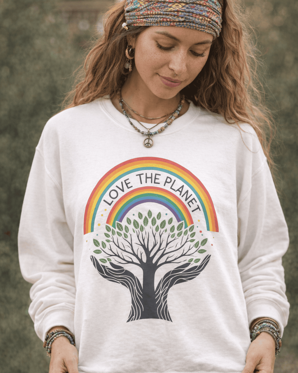 Close-up detail of the Love The Planet crewneck sweatshirt, showing the vibrant rainbow and intricate Tree of Life design. The model complements the pullover's earthy vibe with bohemian accessories and a peace sign necklace.