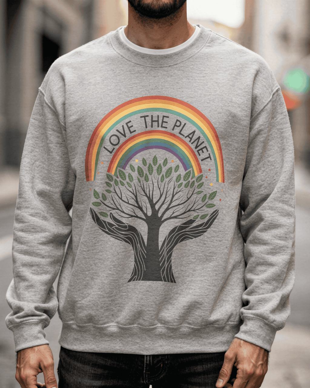 A detailed close-up of the Sport Grey Love The Planet crewneck sweatshirt. The intricate graphic shows a Rainbow Tree of Life with green leaves, held in two hands, beneath an arching rainbow with the words "LOVE THE PLANET."