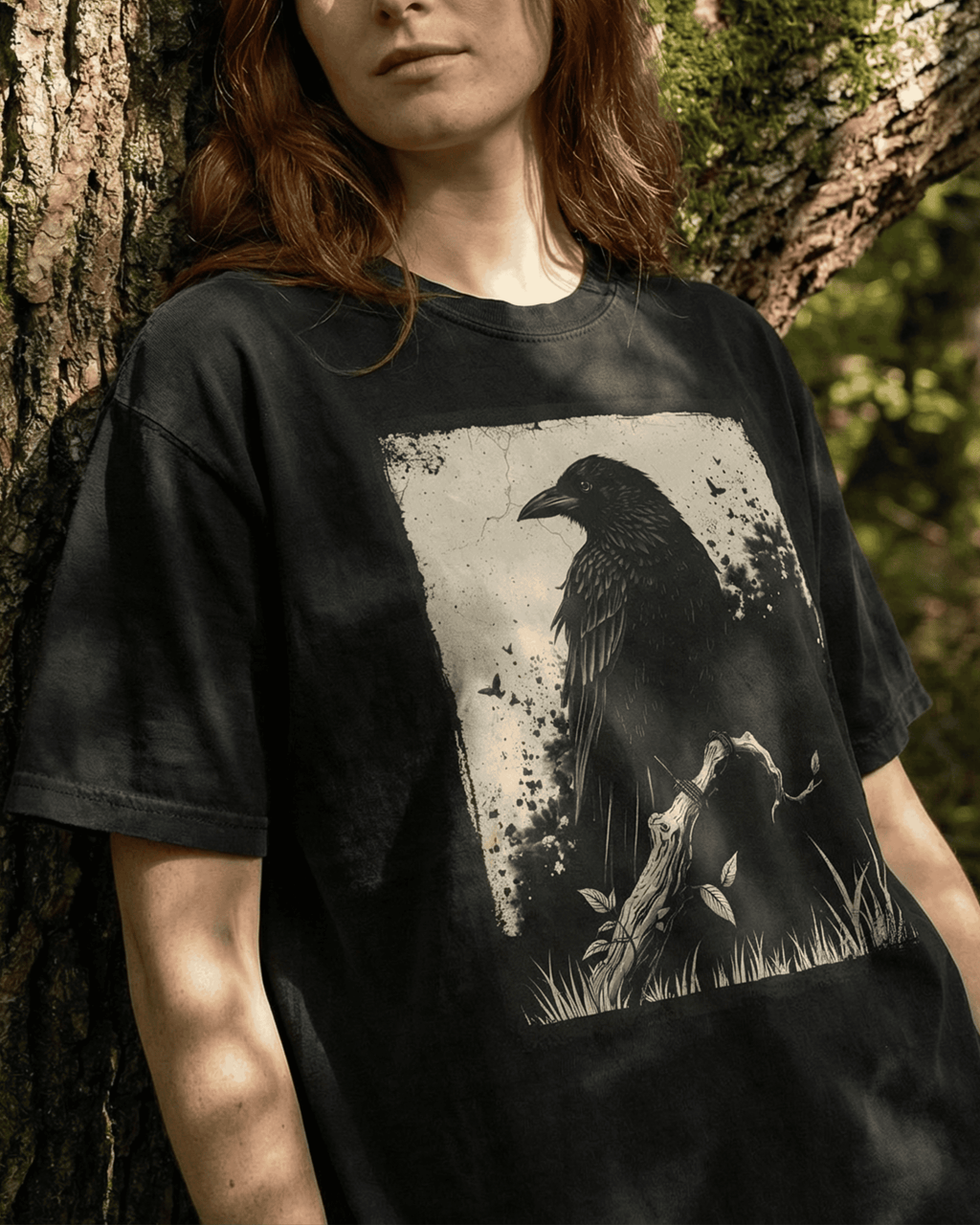  A model wears the black Grunge Witchy Crow T-shirt for women and men, leaning against a tree in a sunlit forest. This Goth Alternative Style Shirt shows off its comfortable, relaxed fit and the detailed raven graphic in a natural, moody setting.
