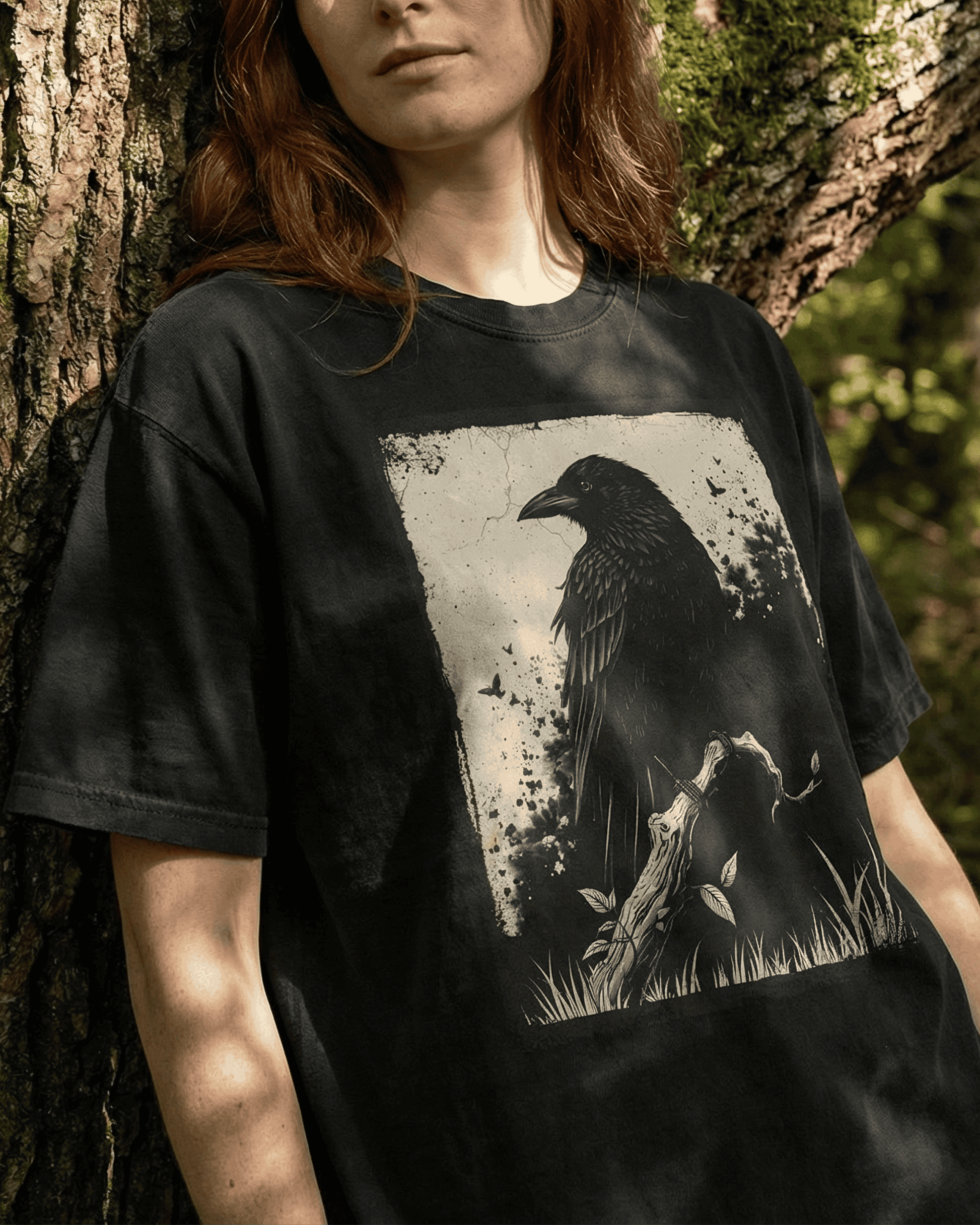  A model wears the black Grunge Witchy Crow T-shirt for women and men, leaning against a tree in a sunlit forest. This Goth Alternative Style Shirt shows off its comfortable, relaxed fit and the detailed raven graphic in a natural, moody setting.