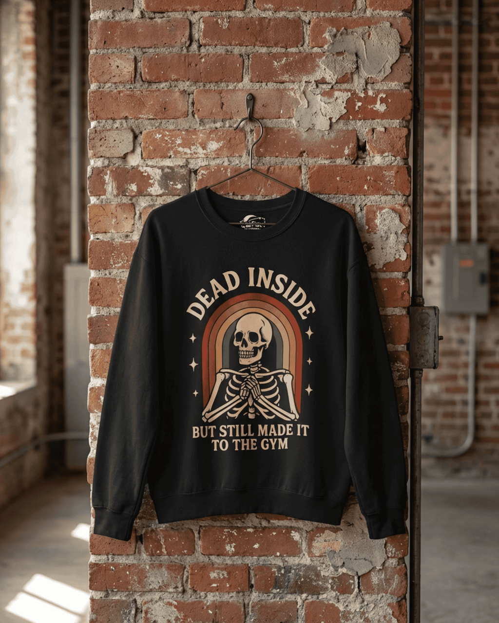 A black Rainbow Skeleton Dead Inside Pullover hanging on a hook against a rustic red brick wall. The full design of this Funny Retro Gym Sweatshirt is visible, showcasing the vintage font and colors.