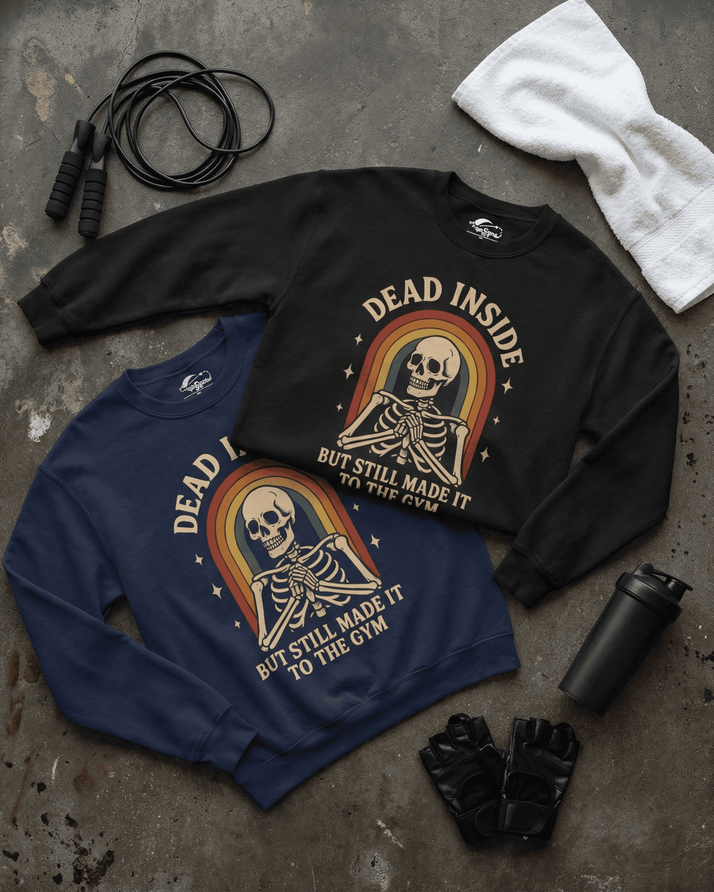 The Funny Retro Gym Sweatshirt shown in both black and navy blue. The Rainbow Skeleton Dead Inside Pullovers are styled in a flat lay with a towel, jump rope, and workout gloves, displaying the available colors for this workout apparel.