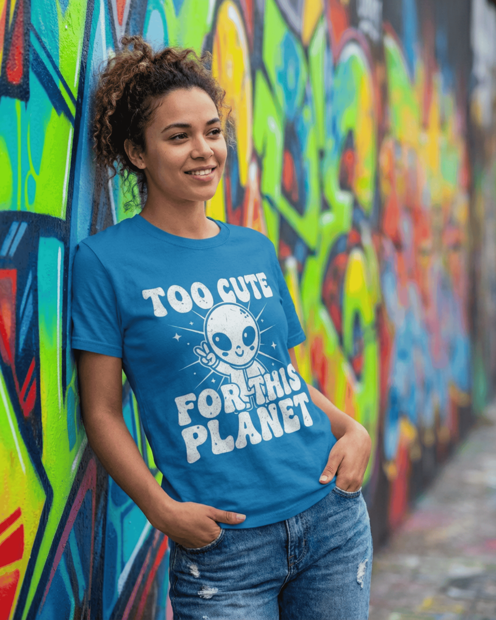 A smiling woman showcases the Retro 90s Y2K Style of this blue UFO Sci Fi Shirt while leaning against a vibrant graffiti wall. This is a trendy and fun graphic tee for teen girls and outer space lovers.