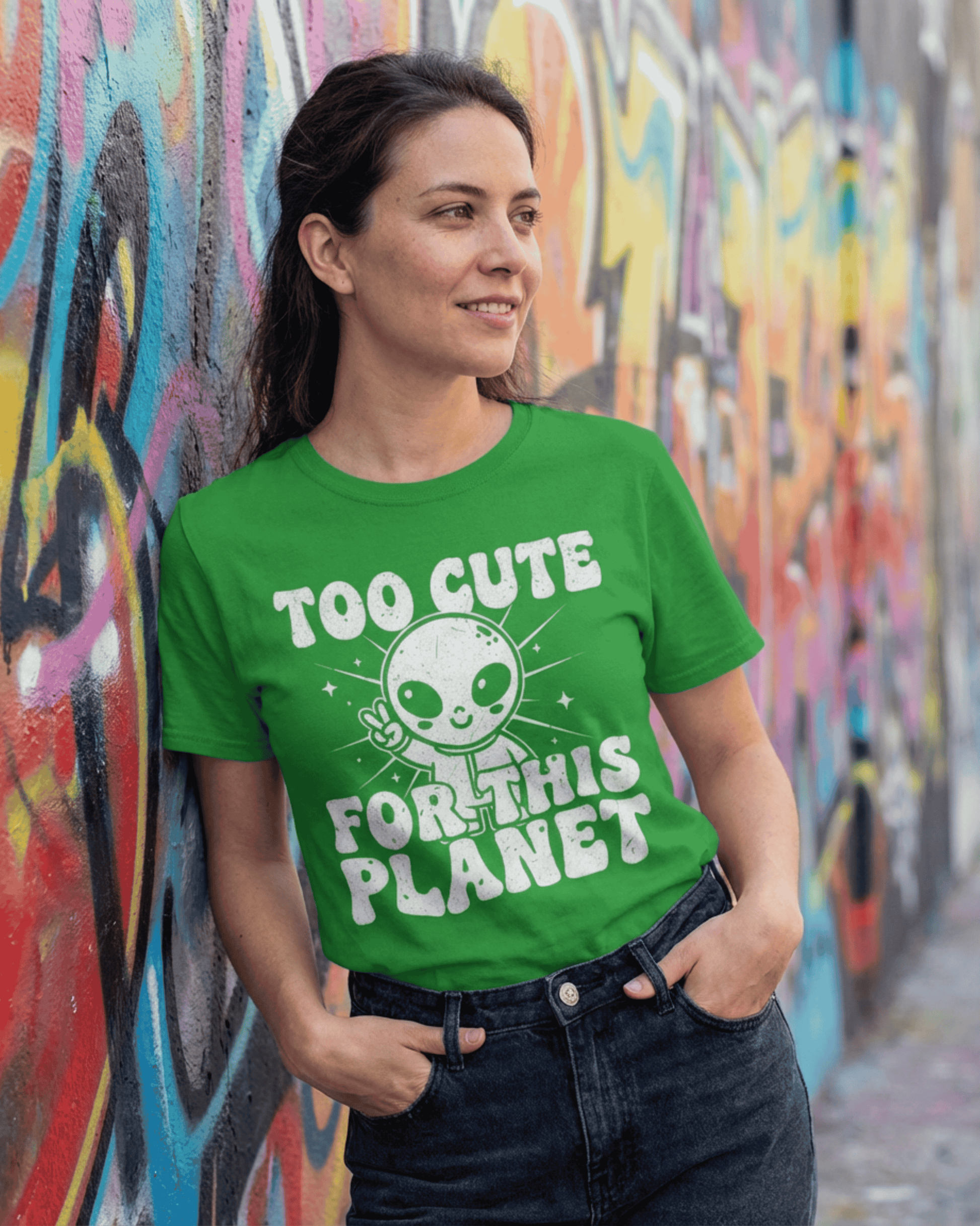 A woman models the green alien graphic tee, showing off its retro 90s Y2K style against a vibrant graffiti wall. This UFO sci-fi shirt is a perfect outer space lover t-shirt for women and teen girls.