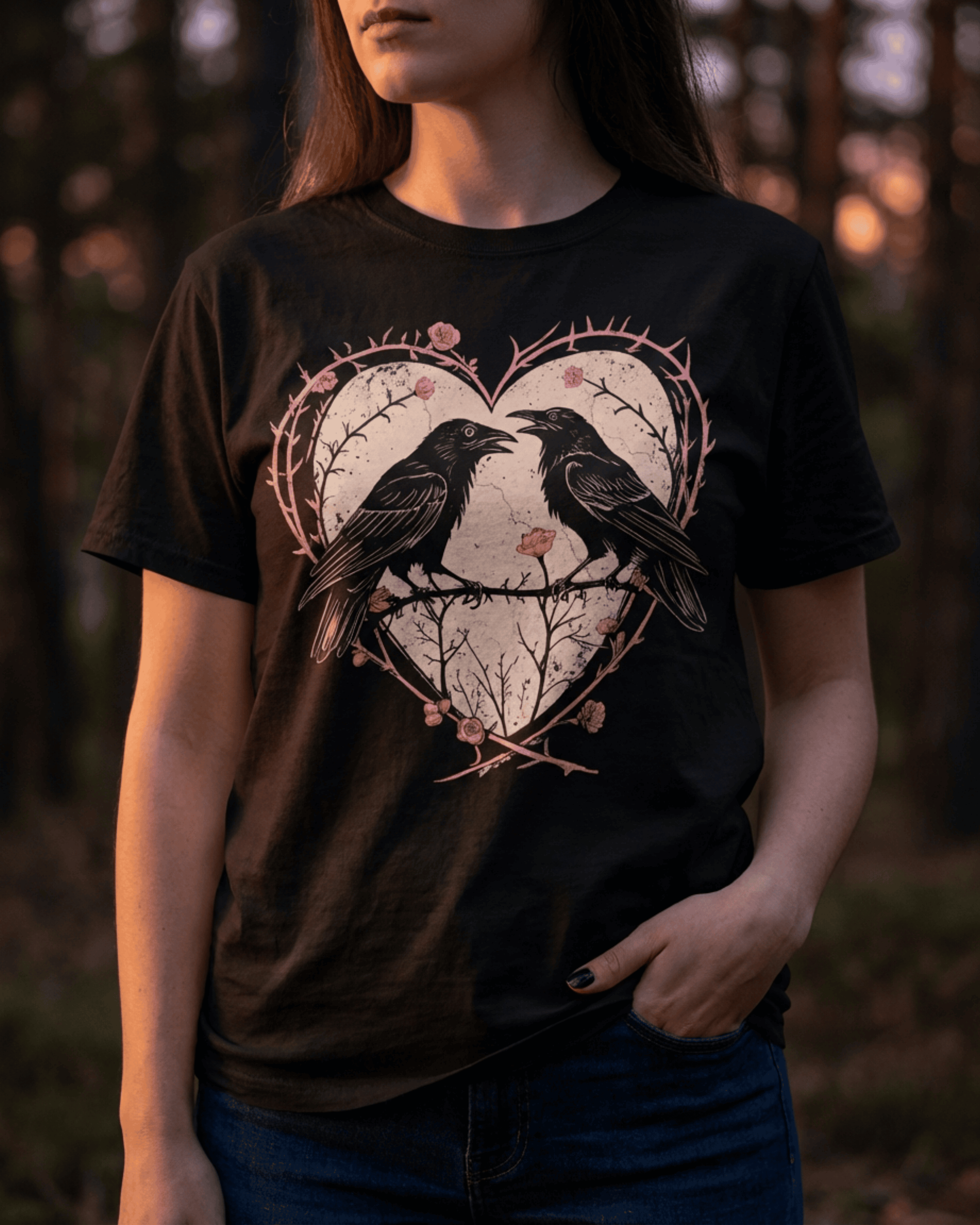 A model wearing the black raven heart shirt, showcasing its Whimsigoth style in a moody forest setting. The edgy punk design, featuring two ravens in a thorny rose heart, perfectly captures a Gothic Dark Romance aesthetic and shows the tee's fit when worn.