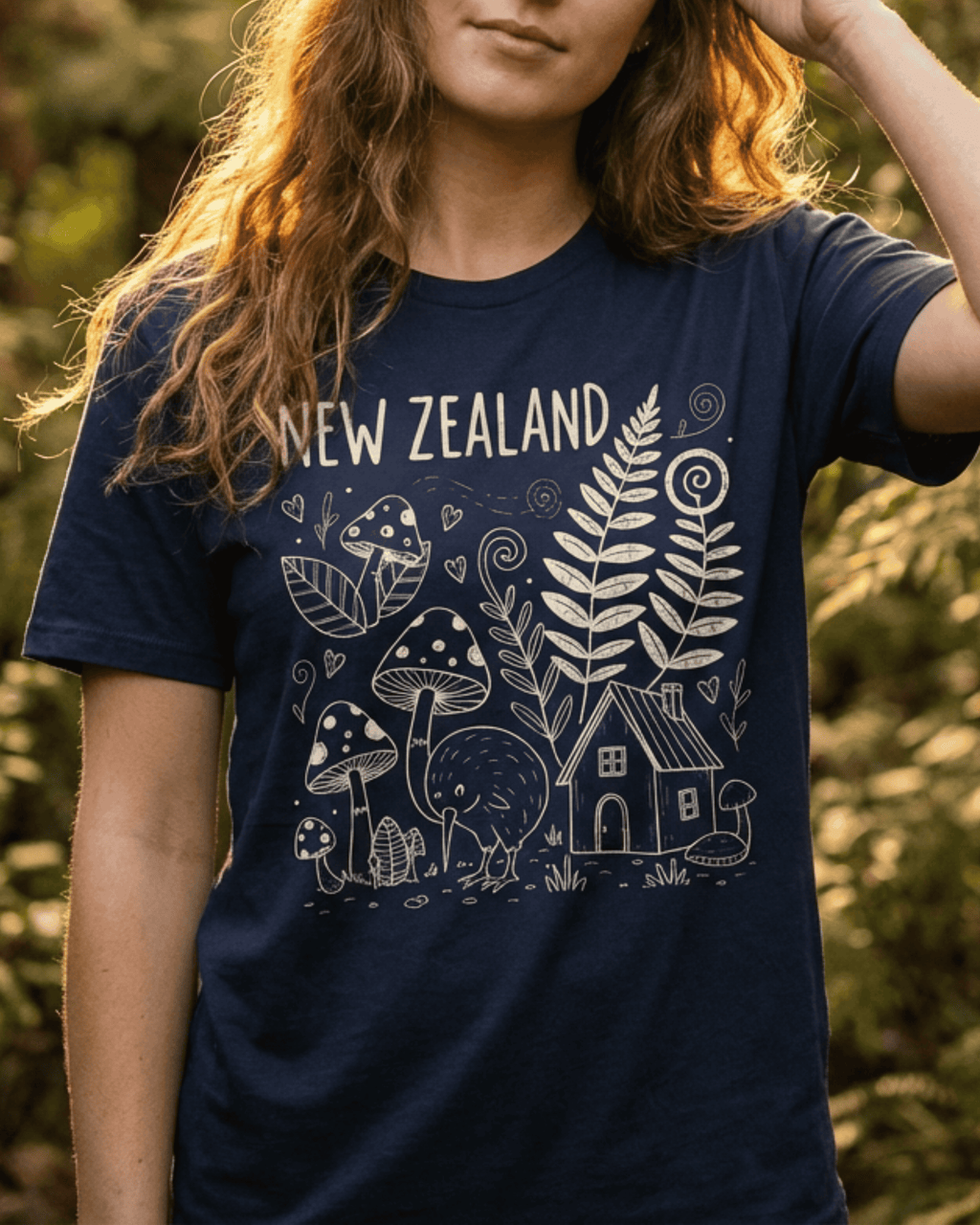 A woman wearing the navy blue New Zealand Tshirt in a lush, green outdoor setting. The cream-colored Kiwi Bird doodle graphic is featured prominently, making this an ideal souvenir shirt for a nature lover. This travel top perfectly expresses NZ Pride while exploring Aotearoa.