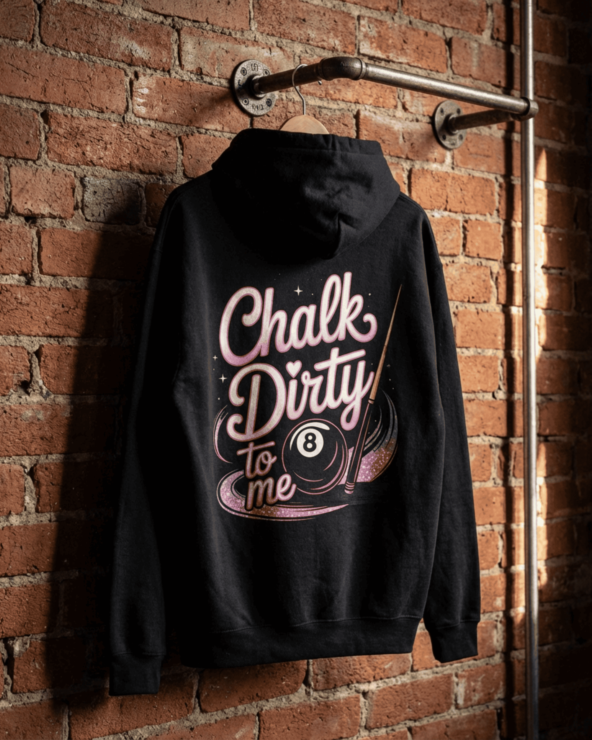 The black Women's Billiards Pool Player Hoodie hanging on a brick wall. The back features the 'Chalk Dirty to me' design in pink, a perfect hooded sweatshirt for any female player.